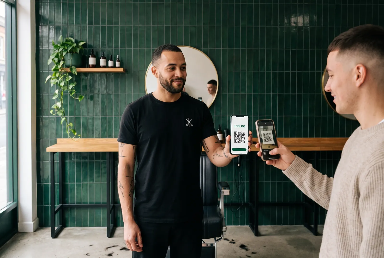A barber showing a £25 QR payment screen on his phone while a customer scans it